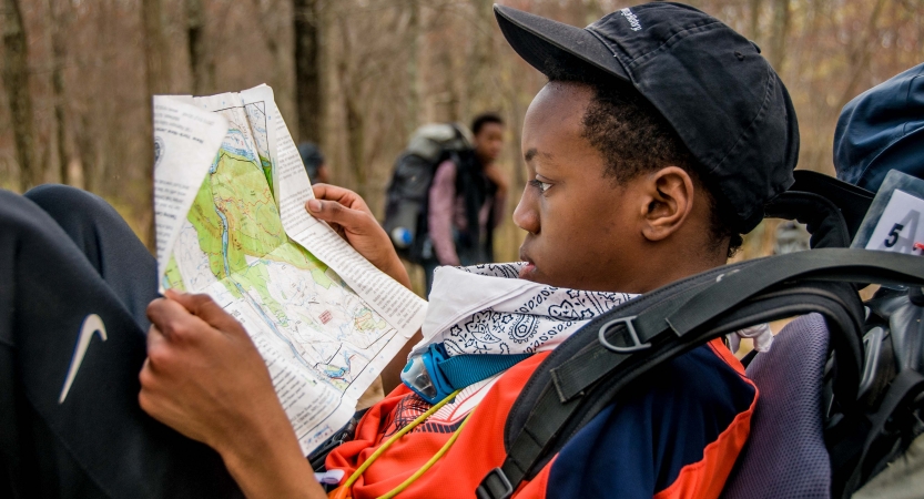 A person rests on the ground and examines a map. 